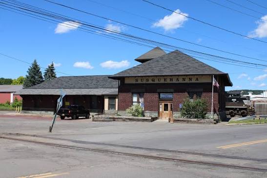 Wide daytime view of the Susquehanna Station with its restored roof, brick walls, and railroad tracks in the foreground.